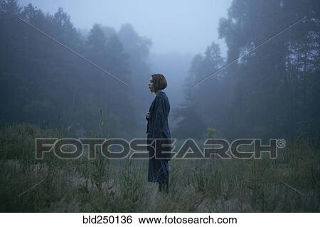 Stock Photograph - Pensive woman standing in fog in forest. Fotosearch