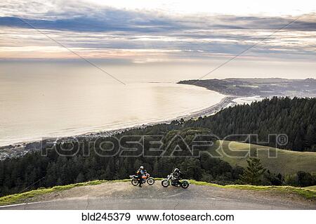 Stock Photo - People on motorcycles at edge of cliff near ocean. Fotosearch