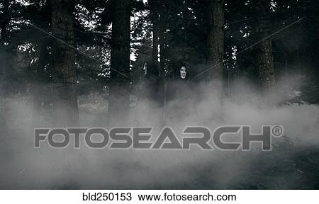 Stock Image - People wearing black robes and white masks in foggy forest. Fotosearch