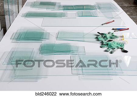 Stock Image - Piles of glass and glass cutter on white table. Fotosearch