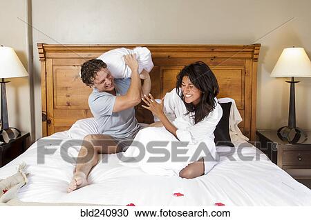 Stock Image - Playful couple having pillow fight on bed. Fotosearch