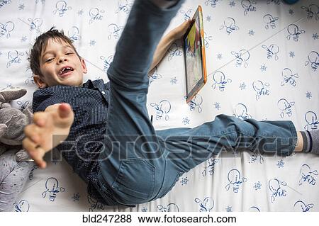 Playful Mixed Race boy laying on bed holding digital tablet View Large Photo Image Stock Photo - Playful Mixed Race boy laying on bed holding digital tablet. Fotosearch