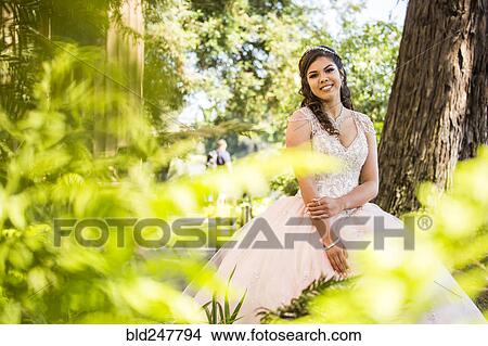 Picture - Portrait of a smiling Hispanic girl wearing gown near foliage. Fotosearch