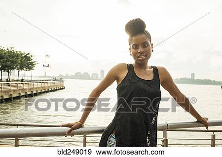 Stock Photo - Portrait of African American woman leaning on railing at waterfront. Fotosearch