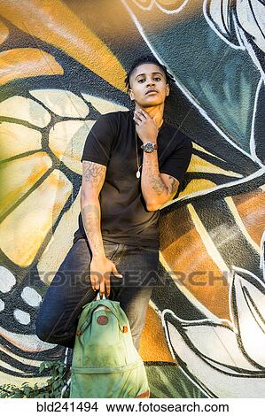 Picture - Portrait of androgynous Mixed Race woman leaning on graffiti wall. Fotosearch