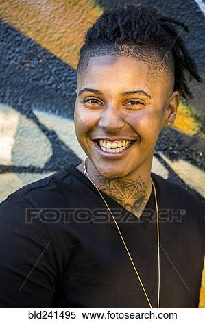 Stock Photography - Portrait of androgynous Mixed Race woman smiling near graffiti wall. Fotosearch