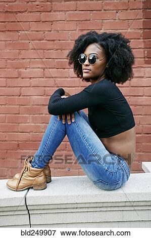 Stock Photo - Portrait of Black woman sitting on ledge outdoors. Fotosearch