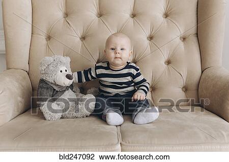 Stock Image - Portrait of Caucasian baby boy sitting on love seat with teddy bear. Fotosearch
