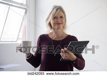 Stock Image - Portrait of Caucasian businesswoman holding coffee cup and digital tablet. Fotosearch