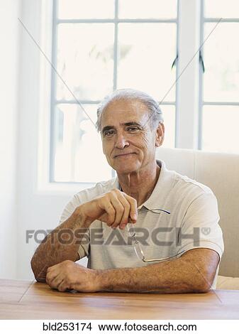 Picture - Portrait of Caucasian man holding eyeglasses at table. Fotosearch