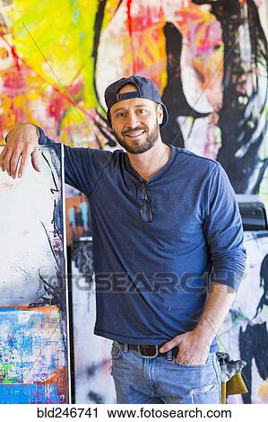 Stock Image - Portrait of Caucasian man leaning on painting. Fotosearch