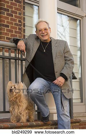 Stock Photo - Portrait of Caucasian man leaning on stoop posing with dog. Fotosearch