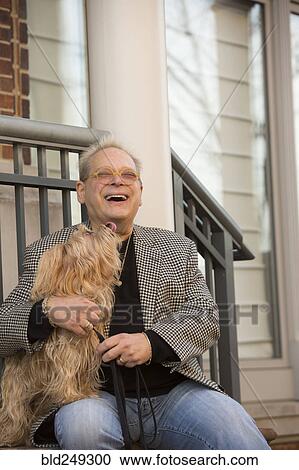 Stock Image - Portrait of Caucasian man sitting on stoop holding dog. Fotosearch