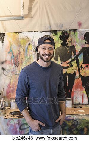 Stock Photograph - Portrait of Caucasian man standing near paintings. Fotosearch