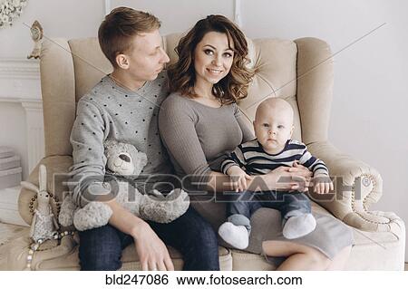 Stock Photograph - Portrait of Caucasian mother and father on love seat with baby son. Fotosearch