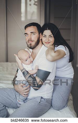 Stock Photography - Portrait of Caucasian mother and father on bed with baby son. Fotosearch