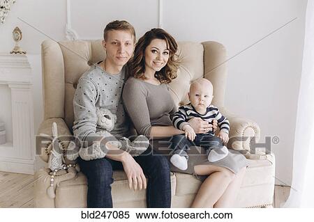 Stock Photography - Portrait of Caucasian mother and father on love seat with baby son. Fotosearch