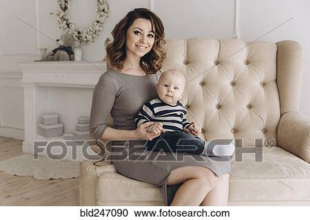 Stock Image - Portrait of Caucasian mother sitting on love seat with baby son. Fotosearch