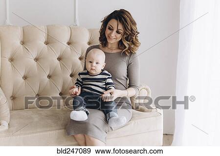 Stock Photo - Portrait of Caucasian mother sitting on love seat with baby son. Fotosearch