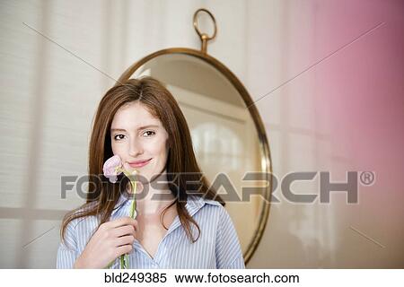 Stock Photography - Portrait of Caucasian woman holding flower near mirror. Fotosearch