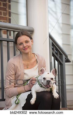 Stock Image - Portrait of Caucasian woman sitting on stoop holding dog. Fotosearch