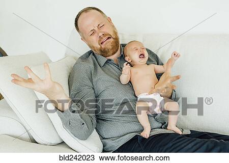 Stock Image - Portrait of crying father holding crying baby daughter. Fotosearch