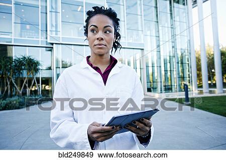 Stock Photo - Portrait of curious Mixed Race doctor holding digital tablet outdoors. Fotosearch