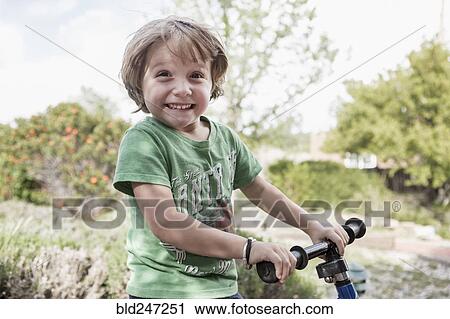 Stock Image - Portrait of excited Caucasian boy holding handlebars. Fotosearch
