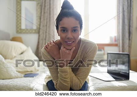 Stock Image - Portrait of Hispanic woman sitting at edge of bed. Fotosearch