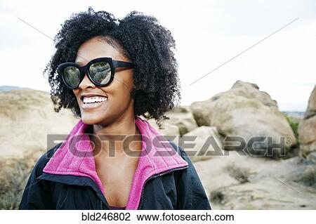 Stock Image - Portrait of laughing Black woman on rock formation. Fotosearch