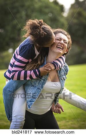Stock Photo - Portrait of laughing girl carrying sister piggyback. Fotosearch