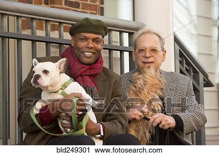 Stock Image - Portrait of men sitting on stoop holding dogs. Fotosearch