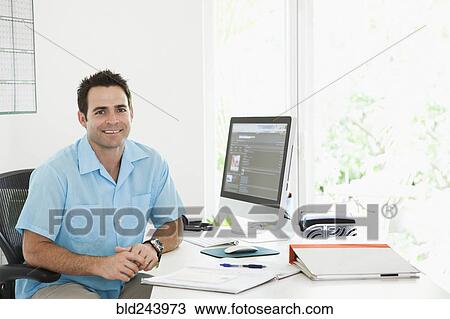 Stock Image - Portrait of Mixed Race man sitting at desk in home office. Fotosearch