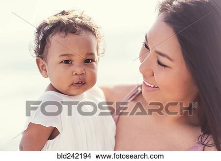 Picture - Portrait of mother holding baby daughter near ocean. Fotosearch