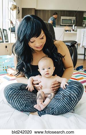 Stock Image - Portrait of mother sitting with baby daughter in lap. Fotosearch