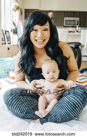 Stock Photo - Portrait of mother sitting with baby daughter in lap. Fotosearch