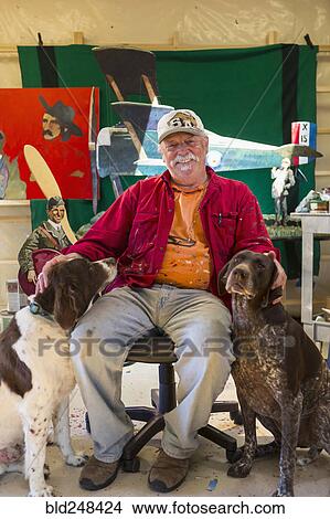 Picture - Portrait of older Caucasian man sitting in workshop with dogs. Fotosearch