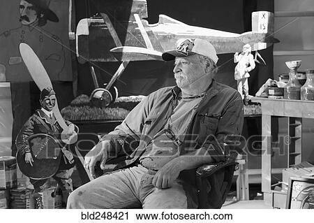Stock Image - Portrait of older Caucasian man sitting in workshop. Fotosearch