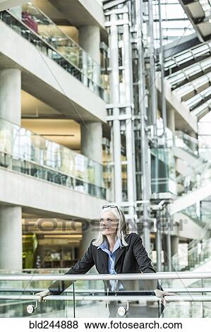 Stock Photo - Portrait of pensive Caucasian businesswoman leaning on railing in lobby. Fotosearch