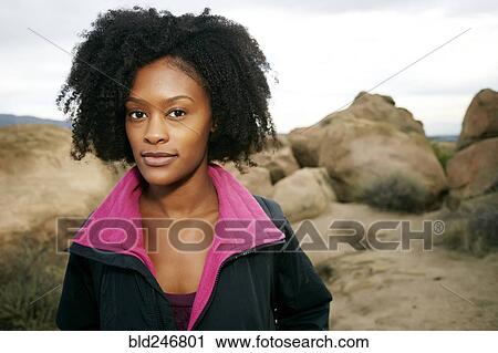 Stock Image - Portrait of serious Black woman posing on rock formation. Fotosearch