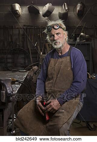 Stock Photo - Portrait of serious Caucasian blacksmith in workshop drinking beer. Fotosearch