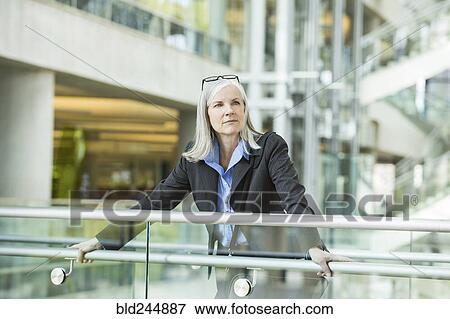 Stock Photo - Portrait of serious Caucasian businesswoman leaning on railing in lobby. Fotosearch