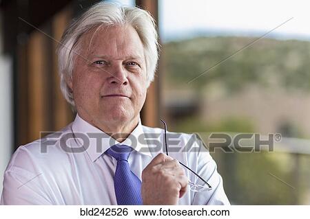 Stock Photograph - Portrait of serious Caucasian businessman holding eyeglasses. Fotosearch