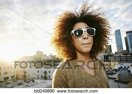 Stock Image - Portrait of serious Hispanic woman on urban rooftop at sunset. Fotosearch