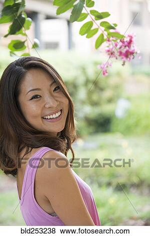 Portrait of smiling Asian woman outdoors near flowers View Large Photo Image Stock Photo - Portrait of smiling Asian woman outdoors near flowers. Fotosearch