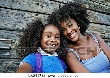 Stock Image - Portrait of smiling Black mother and daughter near wooden wall. Fotosearch