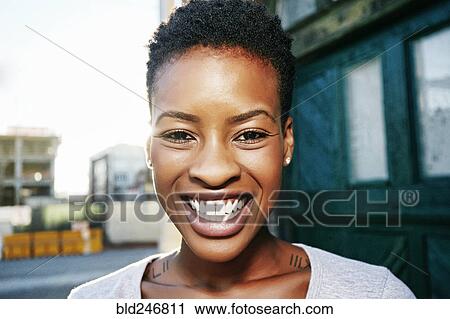 Stock Image - Portrait of smiling Black woman posing in city. Fotosearch