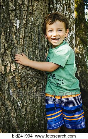 Picture - Portrait of smiling Caucasian boy hugging tree. Fotosearch