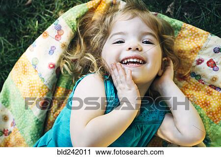 Stock Image - Portrait of smiling Caucasian preschool girl laying on blanket outdoors. Fotosearch