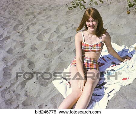 Stock Photograph - Portrait of smiling Caucasian teenage girl sitting on blanket at beach. Fotosearch